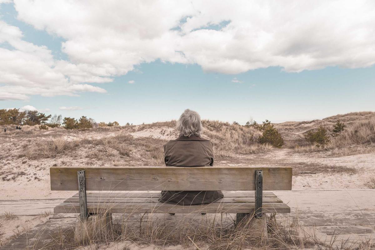 Traveller seated on a bench overlooking coastal dunes - Business Travel Accommodation